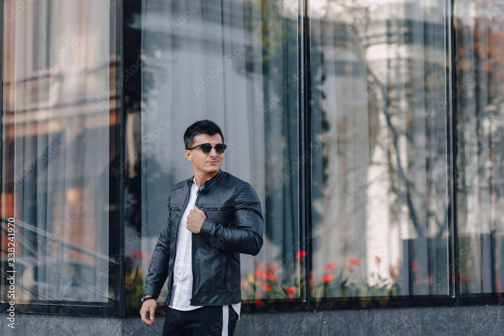 young stylish guy in glasses in black leather jacket on glass background