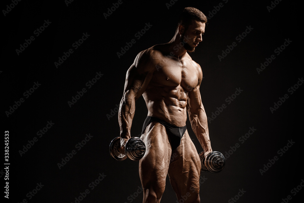 Muscular athletic bodybuilder fitness model posing and training with dumbbells. Isolated on black. Sport photo with dramatic light