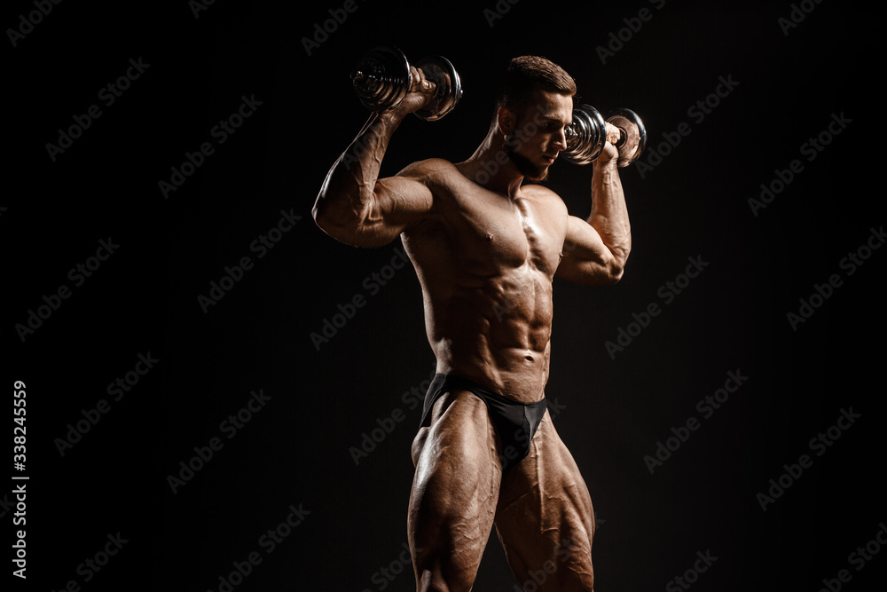 Muscular athletic bodybuilder fitness model posing and training with dumbbells. Isolated on black. Sport photo with dramatic light