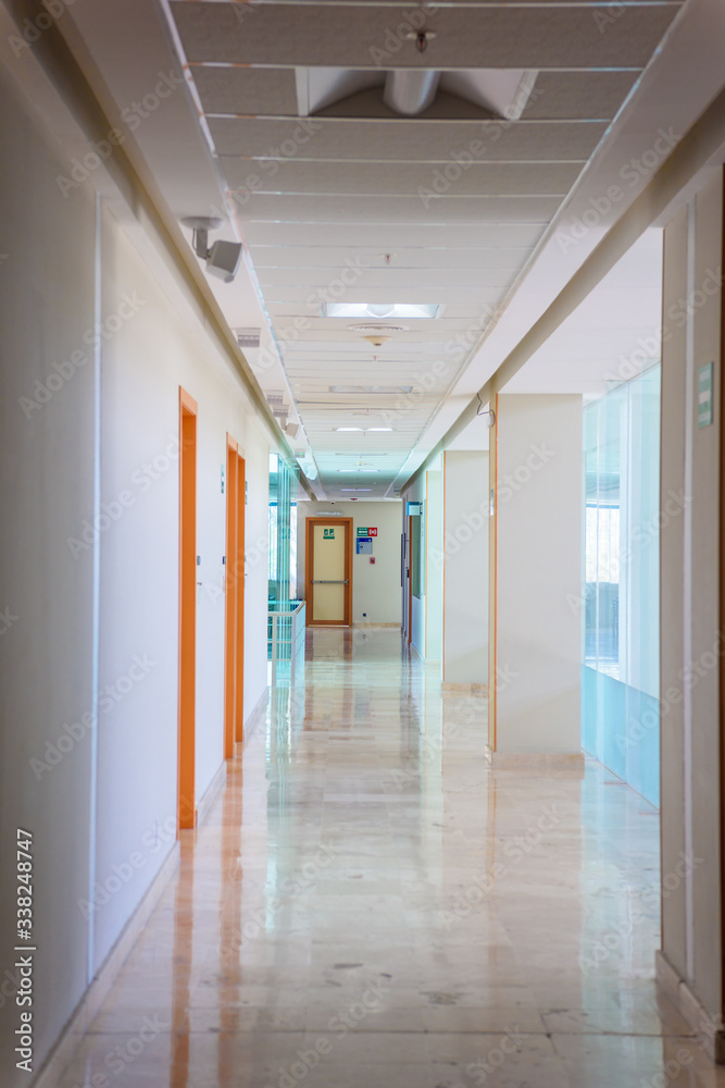 A huge brown door in a white corridor in a hospital.