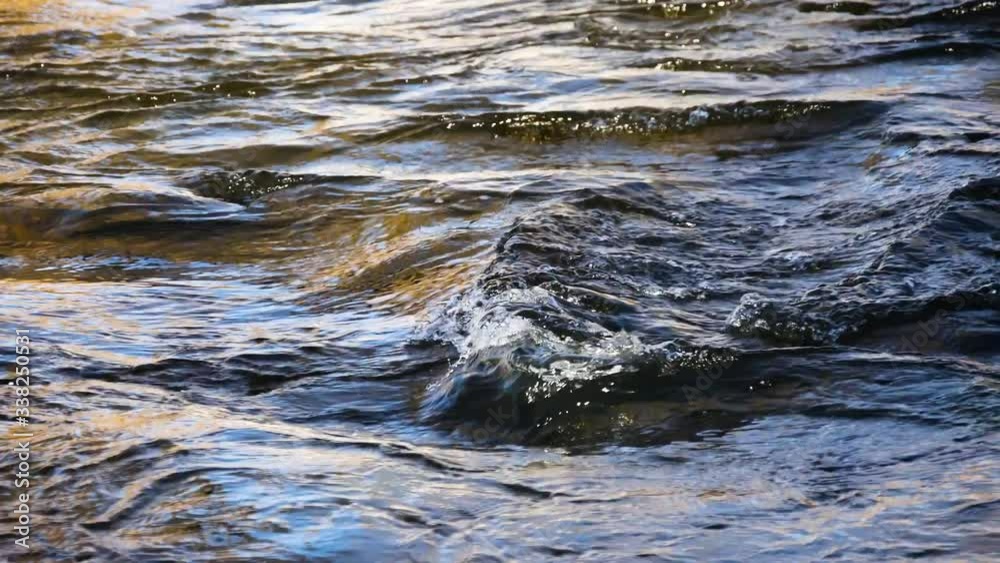 Close video of river water flowing rapidly over shallow rocks in the early morning light. Close video of river water flowing rapidly over shallow rocks in the early morning light.