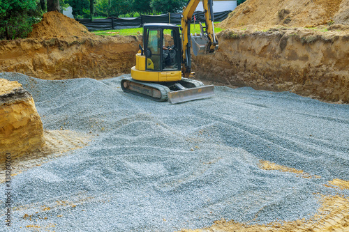 Excavator digging bucket scooping gravel from a building foundation