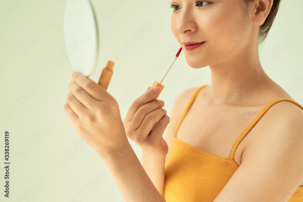 Closeup of Asian young female applying lipstick with mirror against light background. Closeup of Asian young female applying lipstick with mirror against light background.