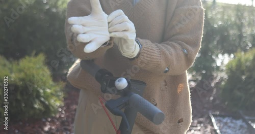 A stylish woman wearing mask and gloves to defened her from coronavirus. Using electric scooter in city and park to be in safe.