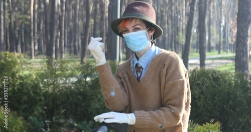 A stylish woman wearing mask and gloves to defened her from coronavirus. Using electric scooter in city and park to be in safe.