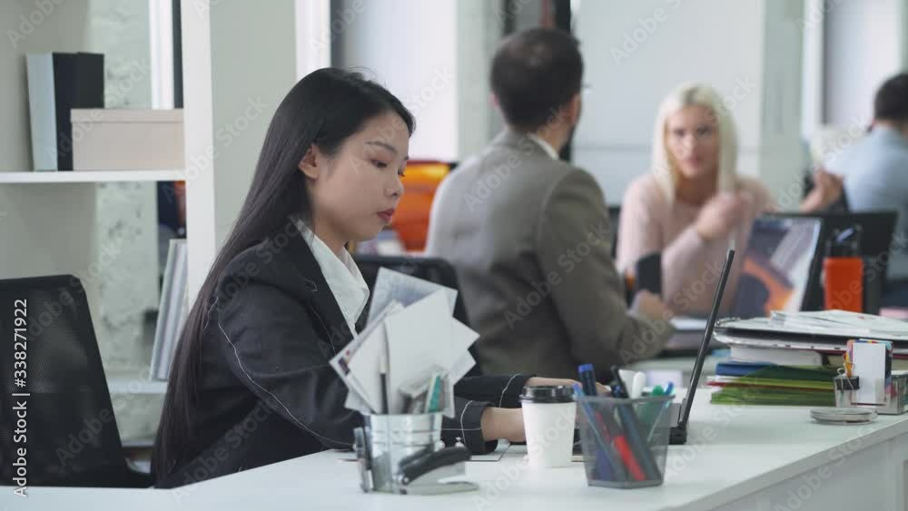 international office, asian woman manager working at the computer, colleagues communicate on a blurry background, working and communicate in an open space. international office, asian woman manager working at the computer, colleagues communicate on a blurry background, working and communicate in an open space.