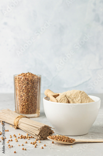 Bowl with gluten free buckwheat flour, buckwheat grains in a glass and soba noodles. Light grey concrete background. Healthy diet. 