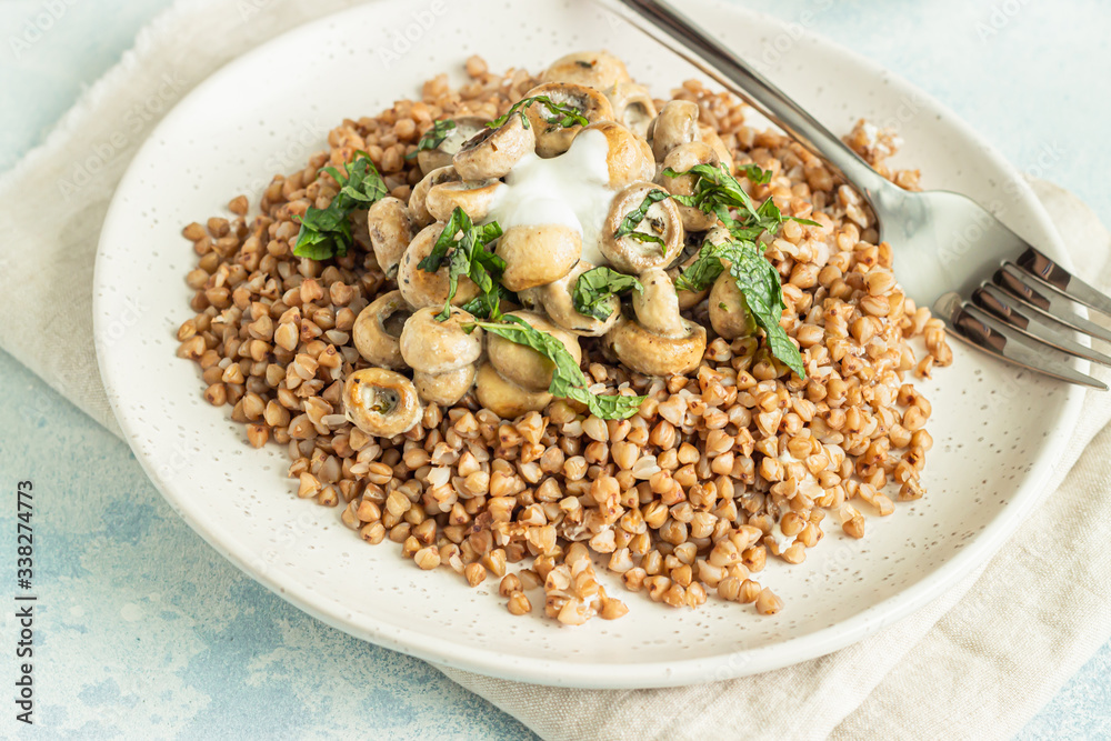 Buckwheat porridge with mushrooms and herbs in a ceramic plate on light grey concrete background. Vegan and vegetarian meal. Healthy content. Toned image. Buckwheat porridge with mushrooms and herbs in a ceramic plate on light grey concrete background. Vegan and vegetarian meal. Healthy content. Toned image.