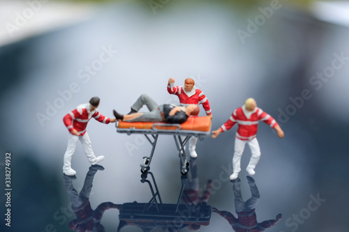 Miniature people : Injured man lying on the first aid bed and there are emergency medical staff dragging a first aid bed. Focused on man who holding salt water line. Emergency, life insurance concept
