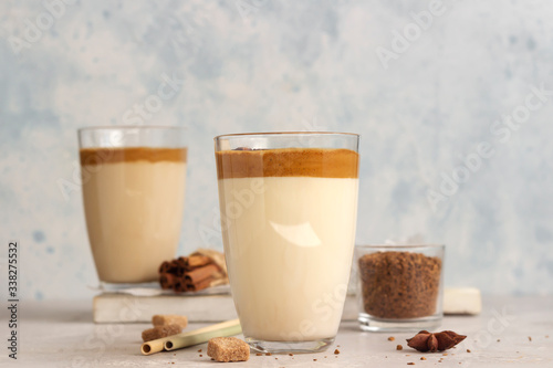 Iced Dalgona coffee in tall glass with spices. A trendy fluffy creamy whipped coffee. Korean coffee drink. Light grey concrete background.