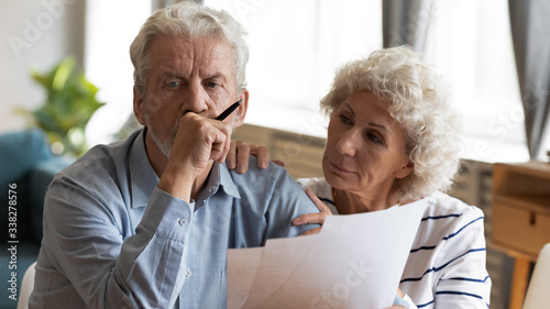 Unhappy older couple reading documents, checking domestic bills, caring mature wife comforting sad upset husband holding debt notification, stressed about financial problem or bankruptcy