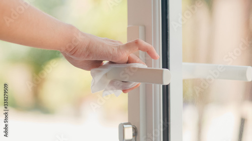 Asian woman using alcohol spray on tissue clean doorknob before open door for protect coronavirus. Female clean surface for hygiene when social distancing stay at home and self quarantine time.