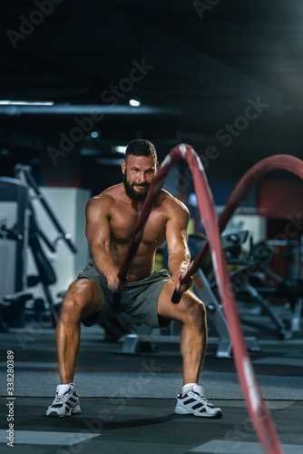 Portrait of strong muscular man pulling heavy rope in gym