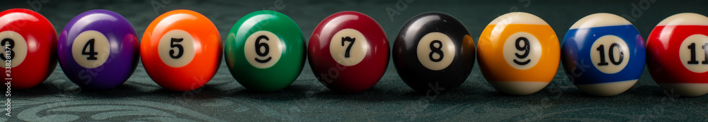 Billiard balls arranged in a row close-up on a green backgound. Wide frame.