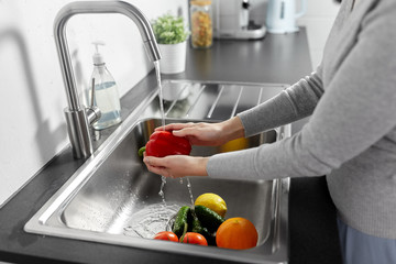 hygiene, health care and safety concept - close up of woman washing fruits and vegetables in kitchen at home