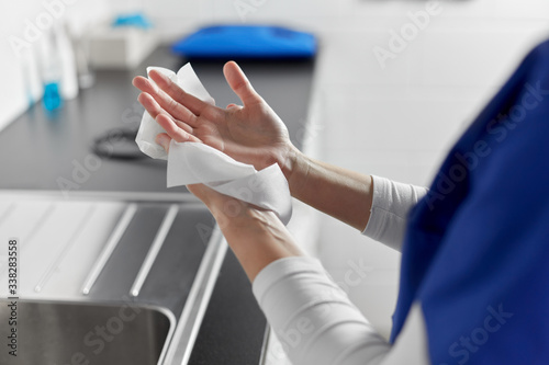 hygiene, health care and safety concept - close up of female doctor or nurse drying hands with paper tissue at hospital