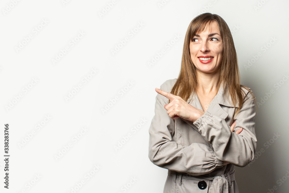 Portrait of a young friendly woman in a classic jacket points a finger to the side and smiles on an isolated light background. Emotional face. Gesture look at it, pay attention