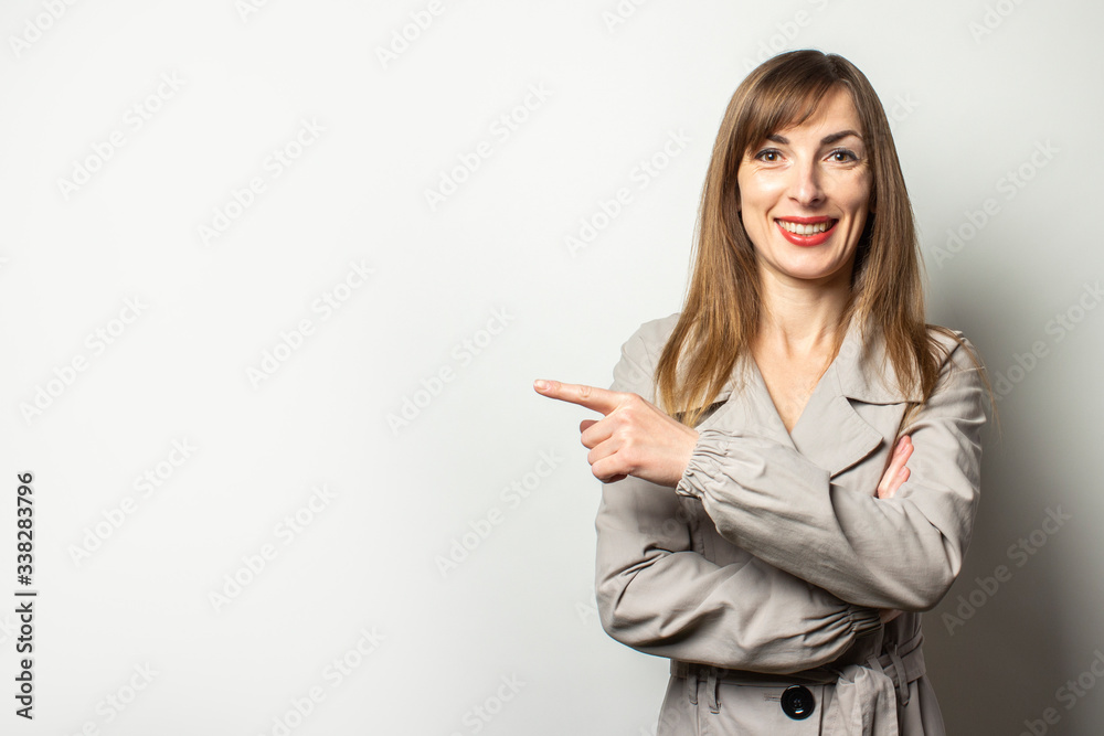 Portrait of a young friendly woman in a classic jacket points a finger to the side and smiles on an isolated light background. Emotional face. Gesture look at it, pay attention Portrait of a young friendly woman in a classic jacket points a finger to the side and smiles on an isolated light background. Emotional face. Gesture look at it, pay attention