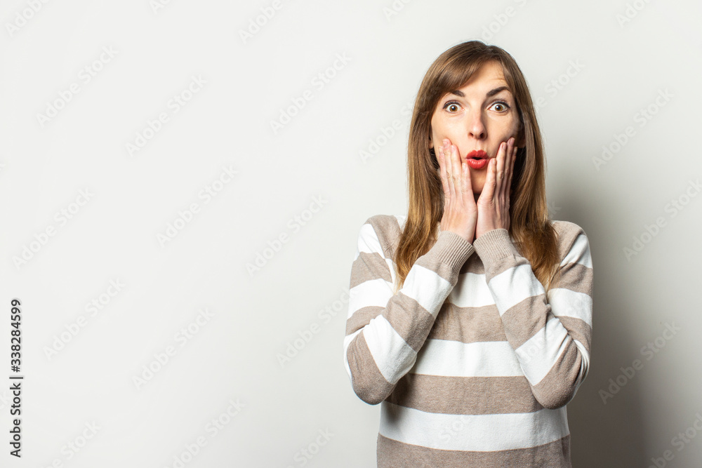 Portrait of a young friendly woman in a striped sweater and a surprised face on an isolated light background. Emotional face. Gesture surprise shock Portrait of a young friendly woman in a striped sweater and a surprised face on an isolated light background. Emotional face. Gesture surprise shock