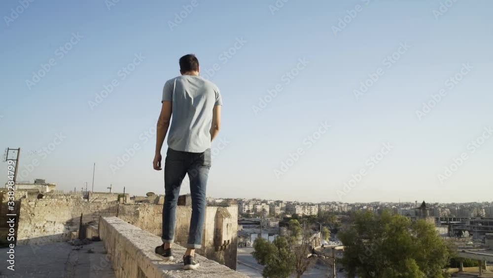 Man walks on edge of roof of building in Aleppo, Syria. Back view real time