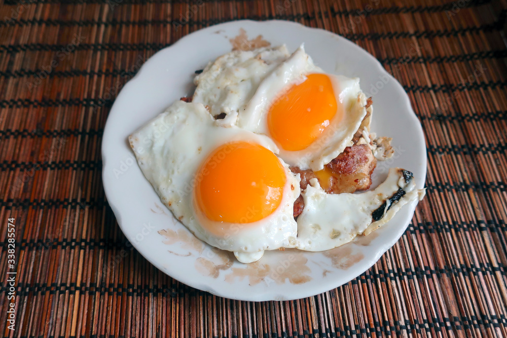 homemade breakfast of fried eggs from two eggs and a piece of fried meat on a plate homemade breakfast of fried eggs from two eggs and a piece of fried meat on a plate