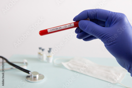 Coronavirus blood test concept. Doctor's hand in a medical glove holding a test tube with positive coronavirus blood over a laboratory desk. Coronavirus COVID-19. Pandemic.