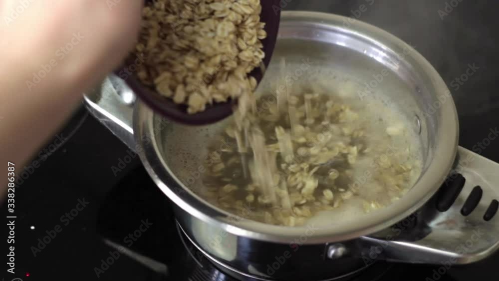 Pouring Oatmeal in boiling water. Preparing oatmeal porridge in the kitchen. Pouring Oatmeal in boiling water. Preparing oatmeal porridge in the kitchen.