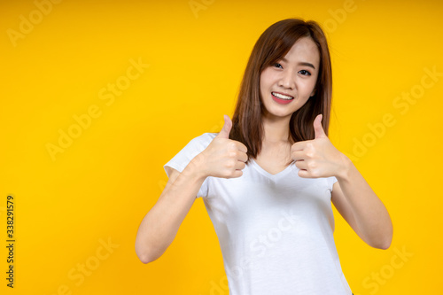 Close up of young Asian woman isolated on yellow background showing thumps up with positive emotions of content and happiness. Copyspace, concept of satisfaction with quality and recommendation.