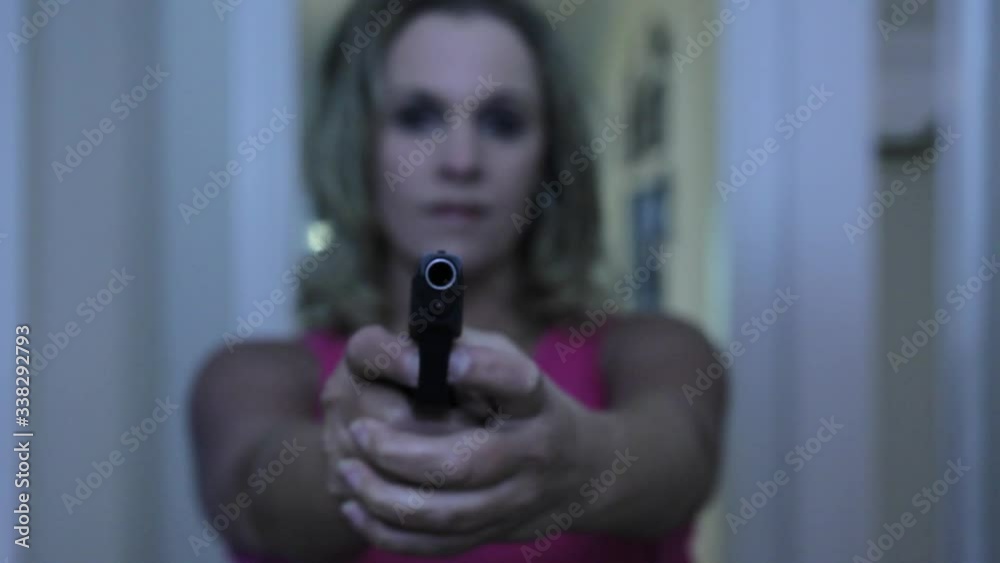 Young Mother pointing a gun at the target hallway in background, selective focus on front of gun Young Mother pointing a gun at the target hallway in background, selective focus on front of gun