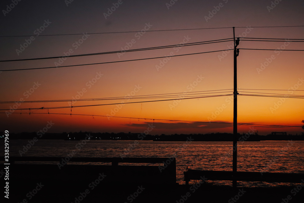 Electricity pylons with wire cable and street lamp post at sunset. River background.