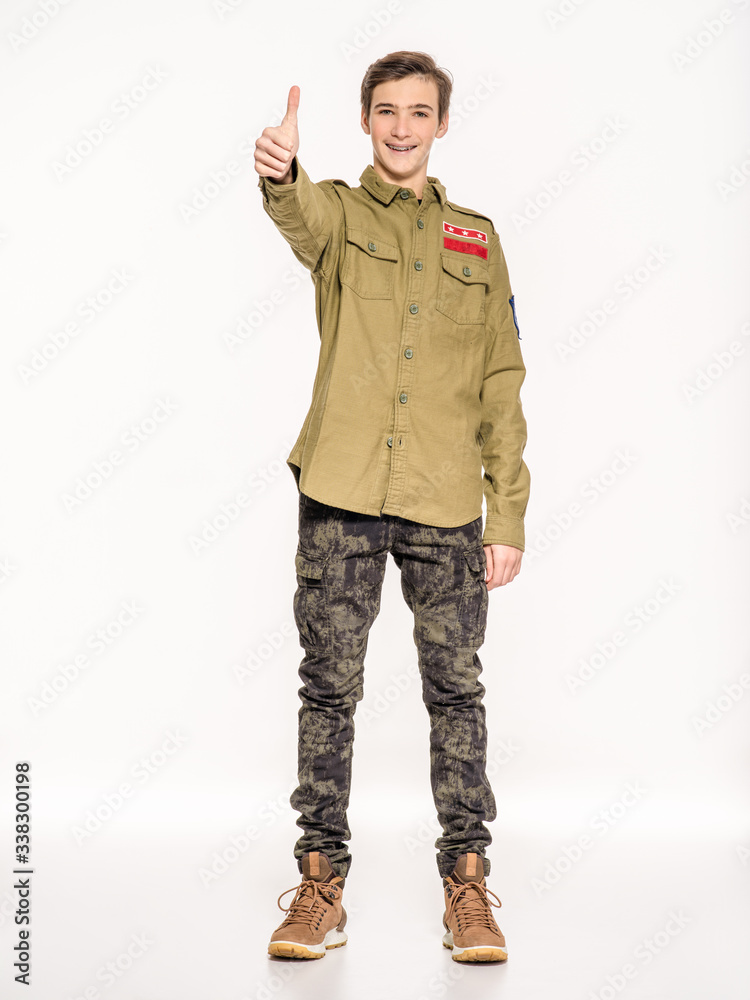 Young man in camouflage clothing shows big thumbs up. Rookie in army clothes. Teenager in khaki military clothing. Conscript in camouflage is showing big thumb. Young man in camouflage clothing shows big thumbs up. Rookie in army clothes. Teenager in khaki military clothing. Conscript in camouflage is showing big thumb.