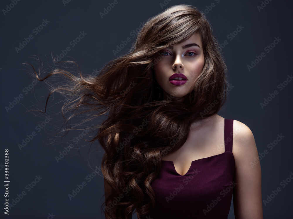 Face of a beautiful woman with long brown curly hair. Fashion model with  wavy hairstyle. Attractive young girl with curly hair posing at studio.  Female face with purple makeup. Violet make-up. Stock