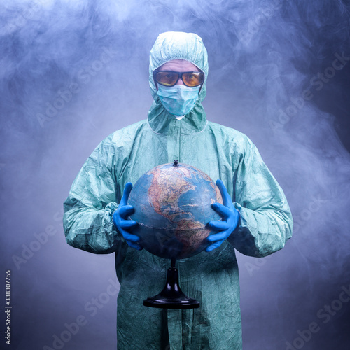 a scientist in a protective suit, blue gloves and yellow glasses holding a globe through the fog