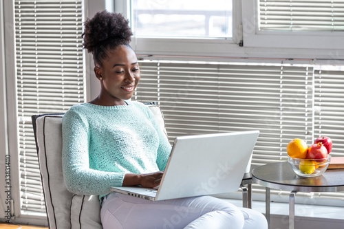 Enjoying time at home. Beautiful young smiling woman working on laptop and drinking coffee while sitting in a big comfortable chair at home photo