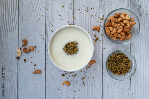 Fototapeta Naklejka Na Ścianę i Meble -  Bowl of cereal matcha oat granola with oat milk, cashew nuts on white wood  Background. vegan food