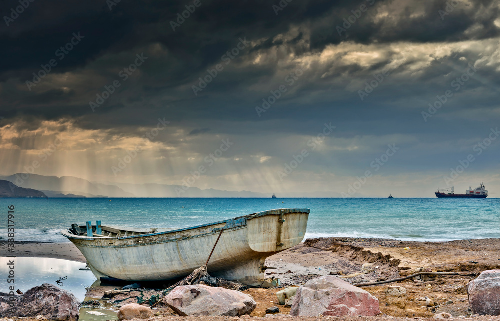 Coastal landscape with old fishing boat abandoned on stone beach after storm, Red Sea Coastal landscape with old fishing boat abandoned on stone beach after storm, Red Sea