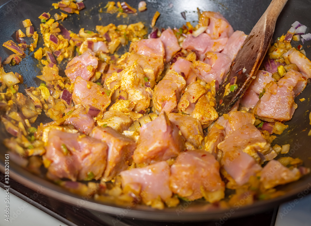 Close up of cubed pork loin, chopped garlic, chopped red onion and a variety of spices frying off in a non-stick pan on the hob whilst making a hot and spicy pork madras curry for dinner Close up of cubed pork loin, chopped garlic, chopped red onion and a variety of spices frying off in a non-stick pan on the hob whilst making a hot and spicy pork madras curry for dinner