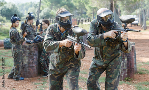 Two men in camouflage holding guns ready for playing paintball with friends