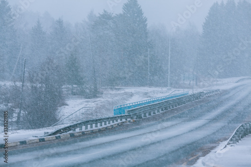 Winter road during snowfall. Bad weather, danger on the road. View of the bridge over the river.