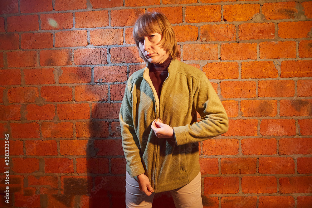 A middle-aged woman poses showing clothes near red brick wall. An inept model in an inept shoot A middle-aged woman poses showing clothes near red brick wall. An inept model in an inept shoot