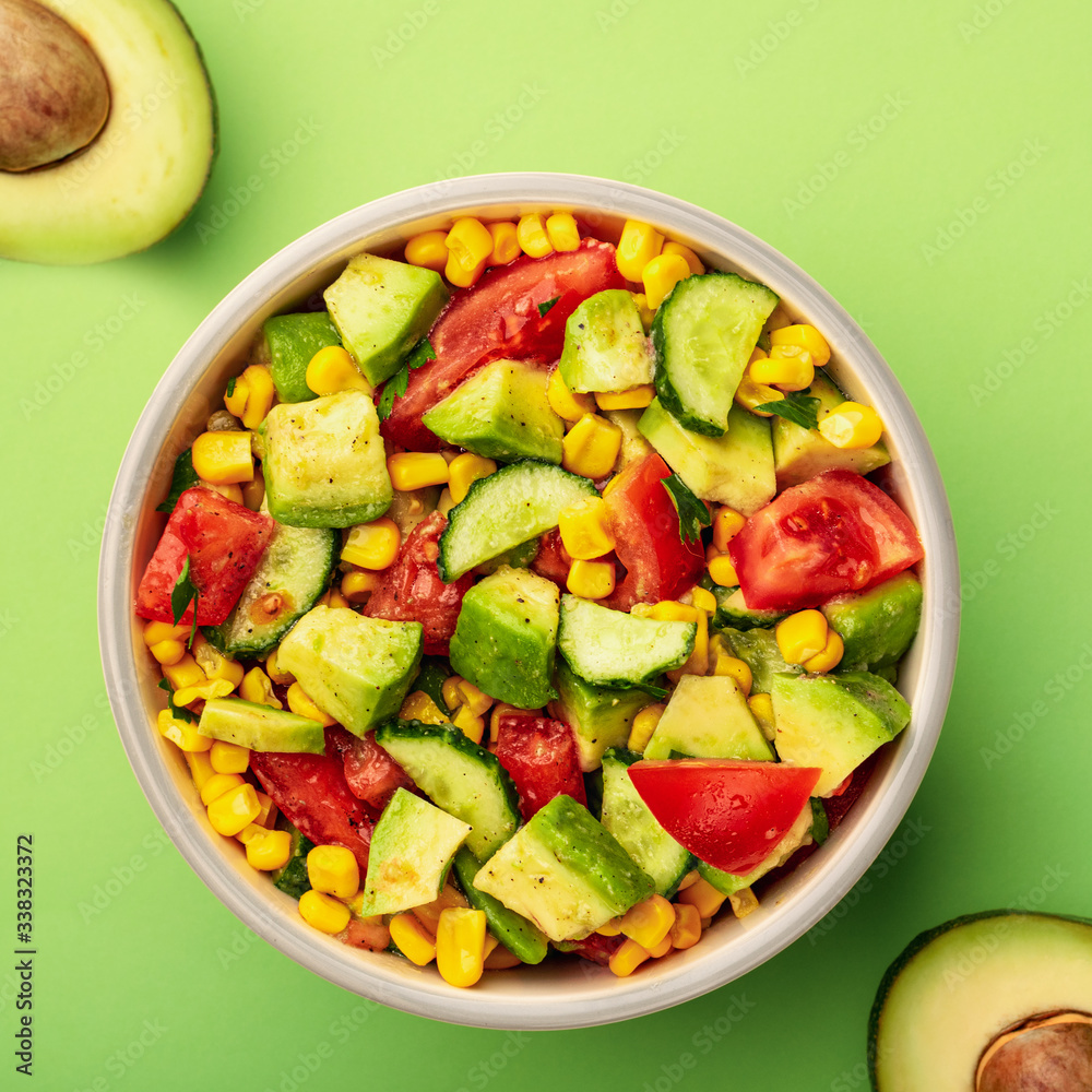 Top view tasty avocado salad with tomatoes, cucumbers in bowl on green background Top view tasty avocado salad with tomatoes, cucumbers in bowl on green background