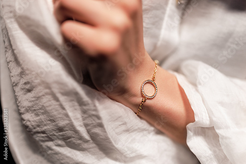 Obraz na płótnie gold bracelet in the form of a ring with diamonds on a chain, girl’s hand, sleeve of a white shirt, dark background