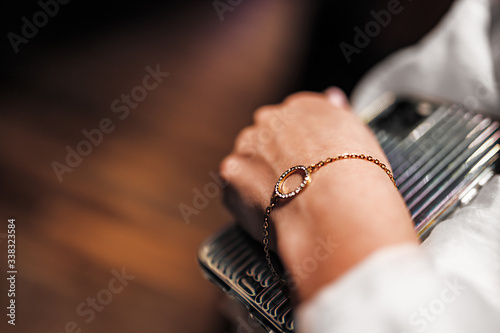 gold bracelet in the form of a ring with diamonds on a chain, girl’s hand, sleeve of a white shirt, dark background. 