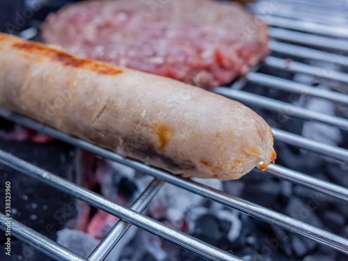 Pork sausage and beef burger on a charcoal BBQ with close up and selective focus on the pork sausage