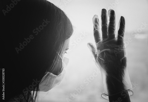 Young woman in medical virus protection face mask and glove near the window. Self-isolation quarantine concept