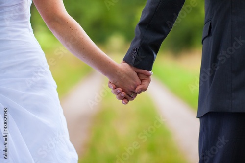 Back view of bride in white dress and groom in suit holding each others hands outdoors Happy bride and groom walking in nature on wedding day. Wedding couple in love, newlyweds, copy space, no face