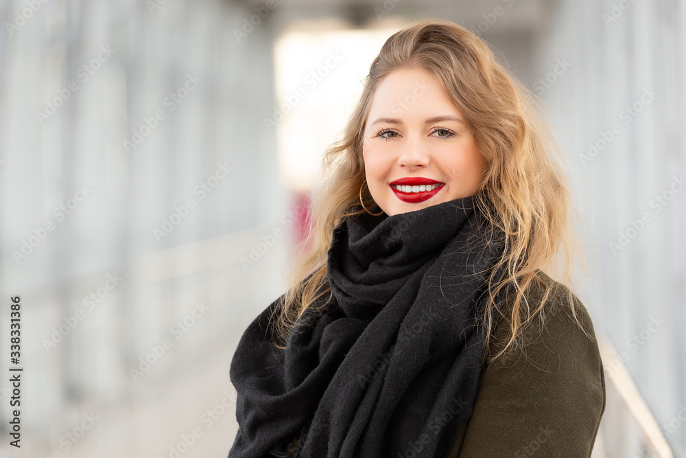 Stylish fashion portrait of blonde woman. Posing in the city. Beautiful girl in autumn green coat and black scarf poses in an overhead pedestrian crossing.