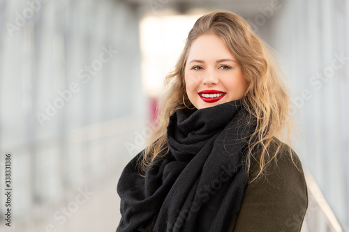 Stylish fashion portrait of blonde woman. Posing in the city. Beautiful girl in autumn green coat and black scarf poses in an overhead pedestrian crossing.