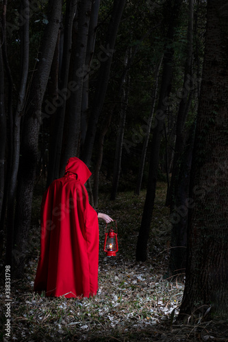 Attractive woman dressed a little red riding-hood walk in a dark forest with lantern