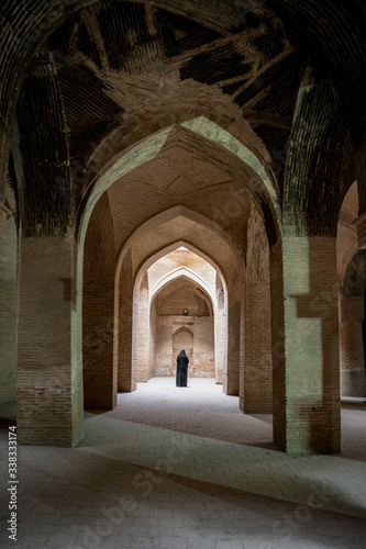 Isfahan, Iran - May 2019: Unidentified iranian woman in hijab black dress walking along the ancient columns of Jameh Mosque of Isfahan